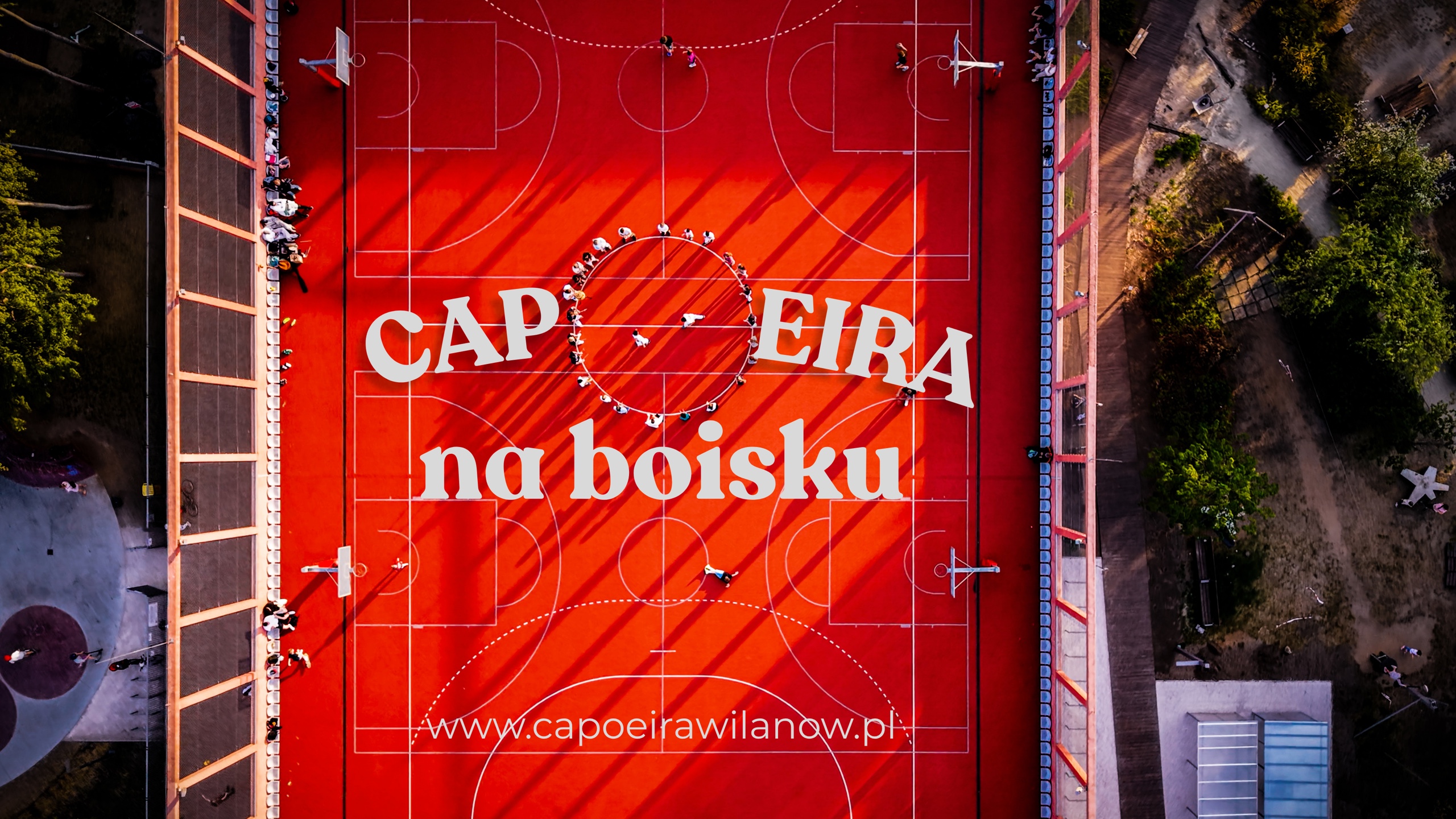 Capoeira na boisku — wakacyjne treningi Capoeira Wilanów, widok z lotu ptaka na Rodę na czerwonym boisku